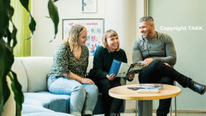 Kaksi naista ja mies istumassa sohvaryhmällä ja tutkimassa opintoesitettä.